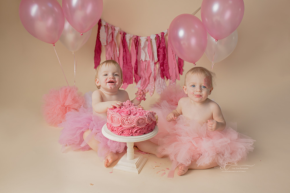 Twin girls smiling playing with cake at their cake smash in Surrey