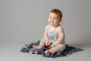 9 month old baby boy wearing blue dungarees with happy expression on his face playing with cars portrait by Horsham photographer