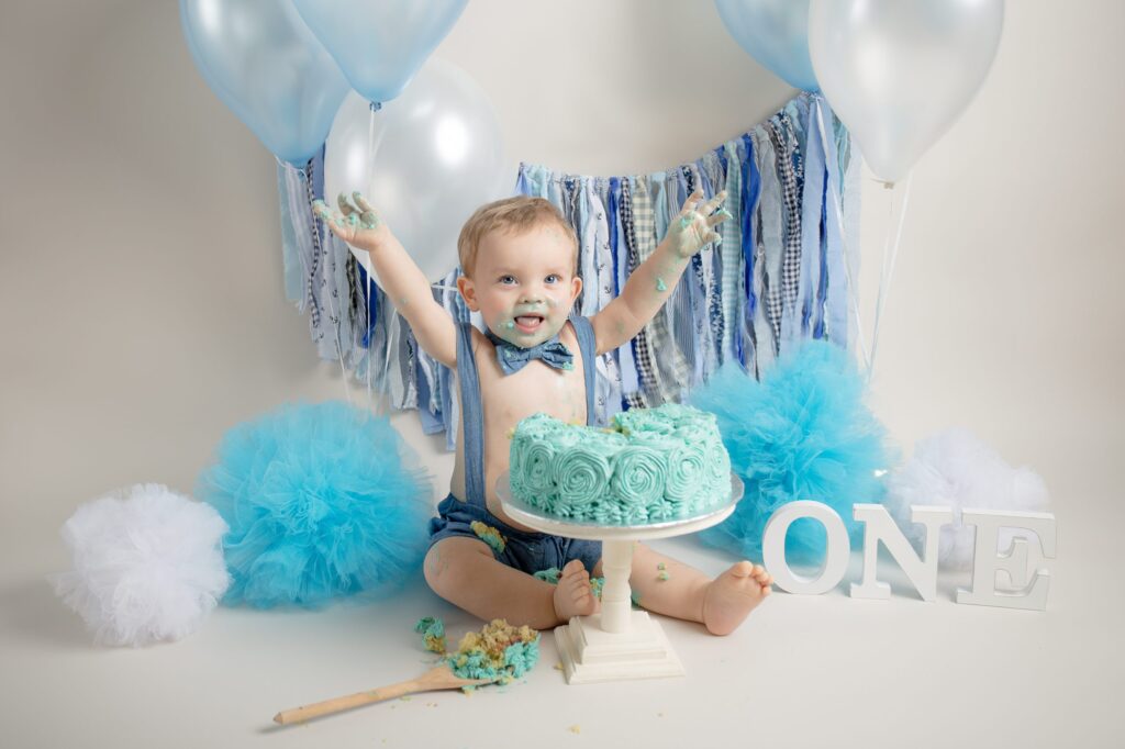 Baby boys waves arms to celebrate his first birthday cake smash in East Grinstead