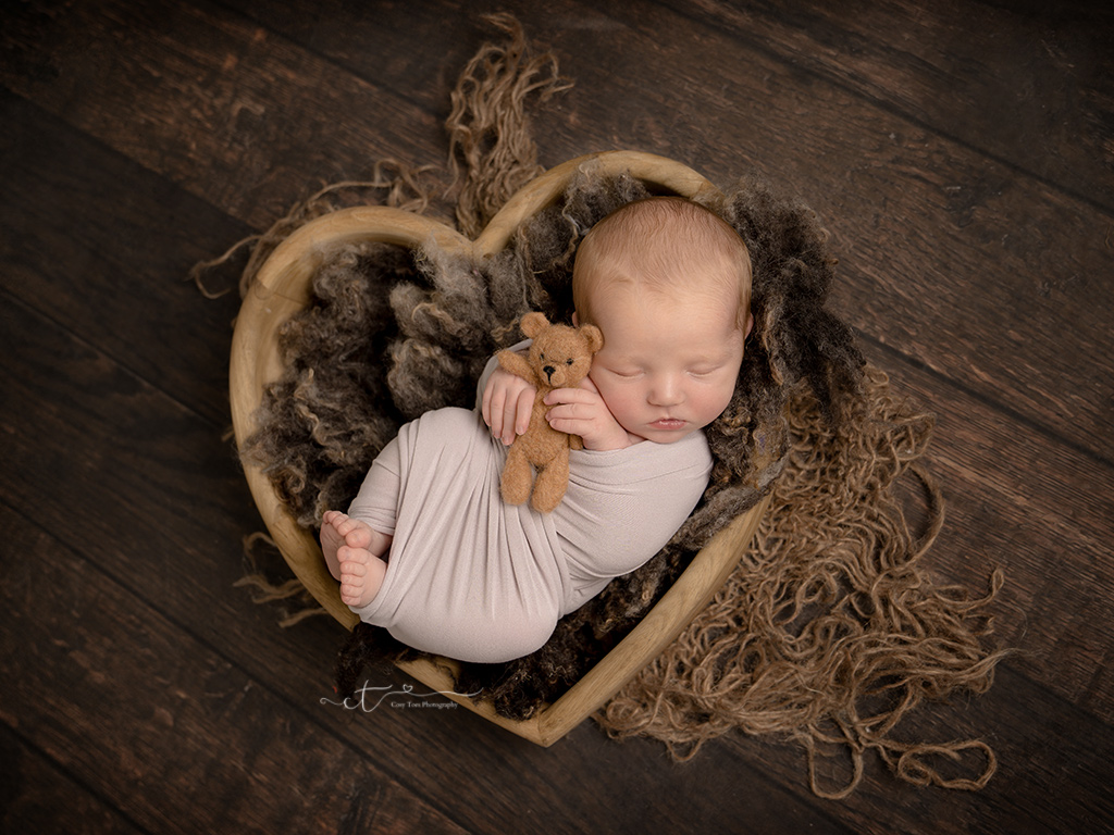 Newborn baby boy swaddled sleeping in heart bowl at his newborn mini photoshoot East Grinstead
