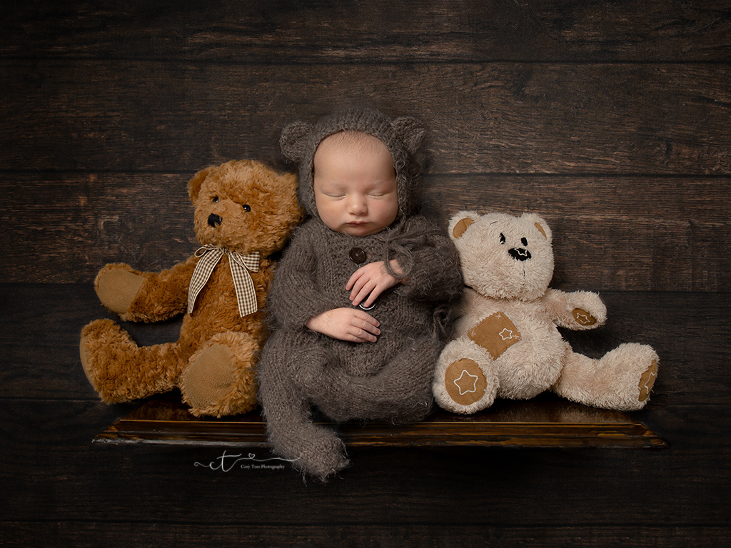newborn baby dressed as tedding sitting on shelf between two other teddies by East Grinstead newborn baby Photographer