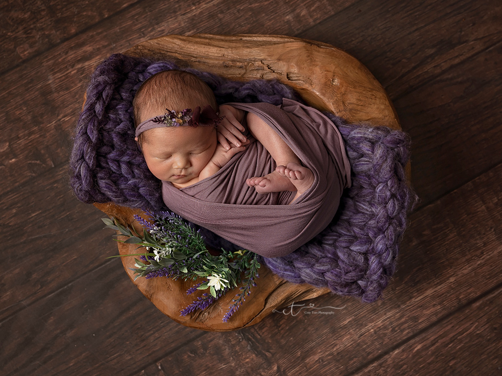 Newborn baby girl swaddled sleeping on wooden bowl at her newborn photoshoot