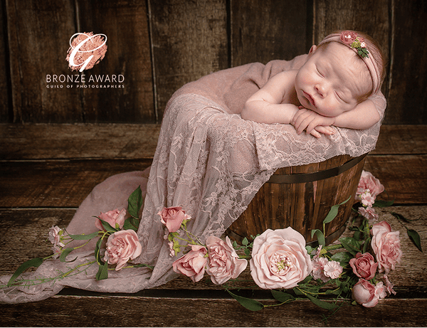 Baby laying in wooden bucket surrounded by flowers by Crawley photographer