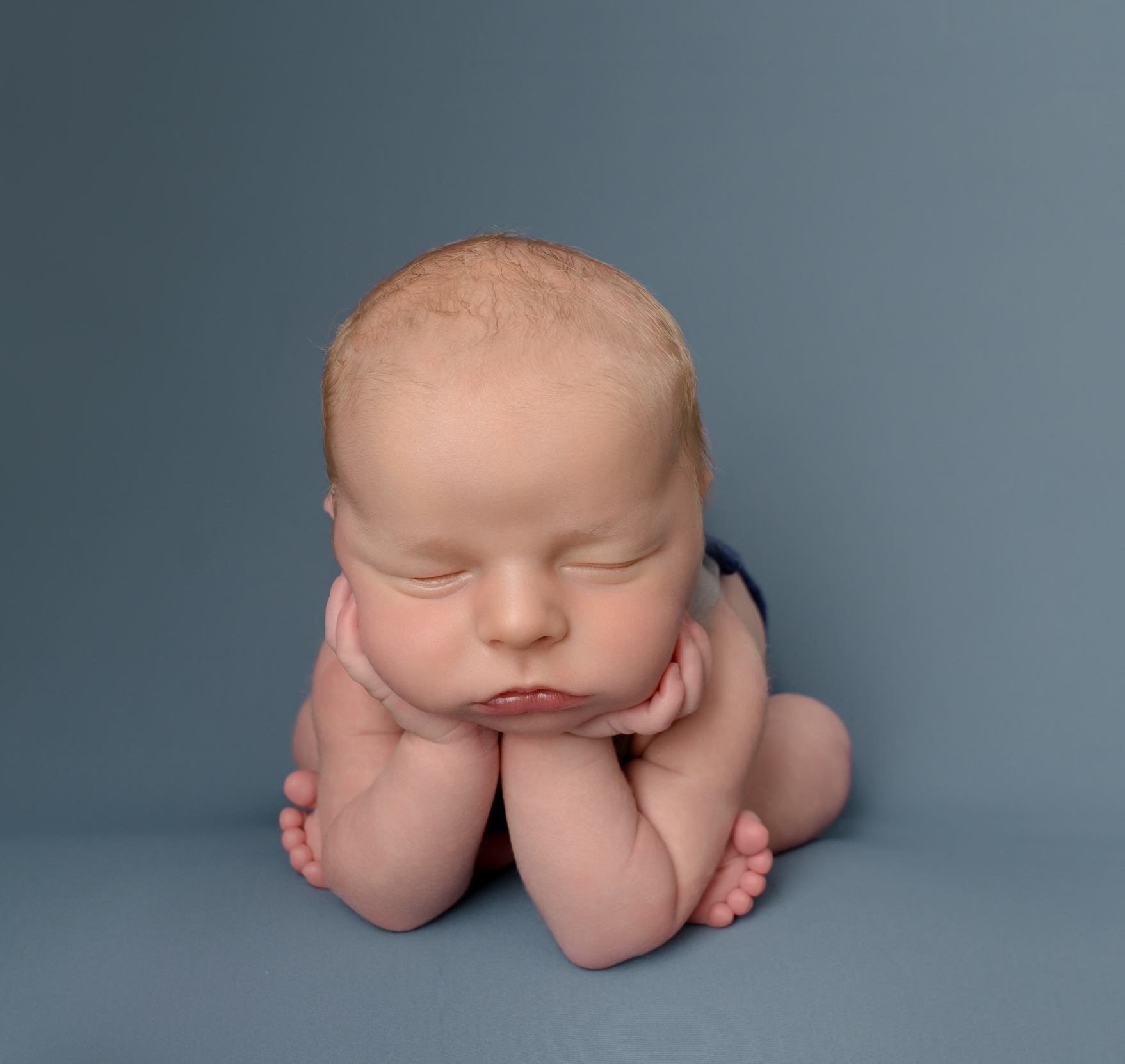 Newborn baby leaning forward with head in hands by Horley photography studio