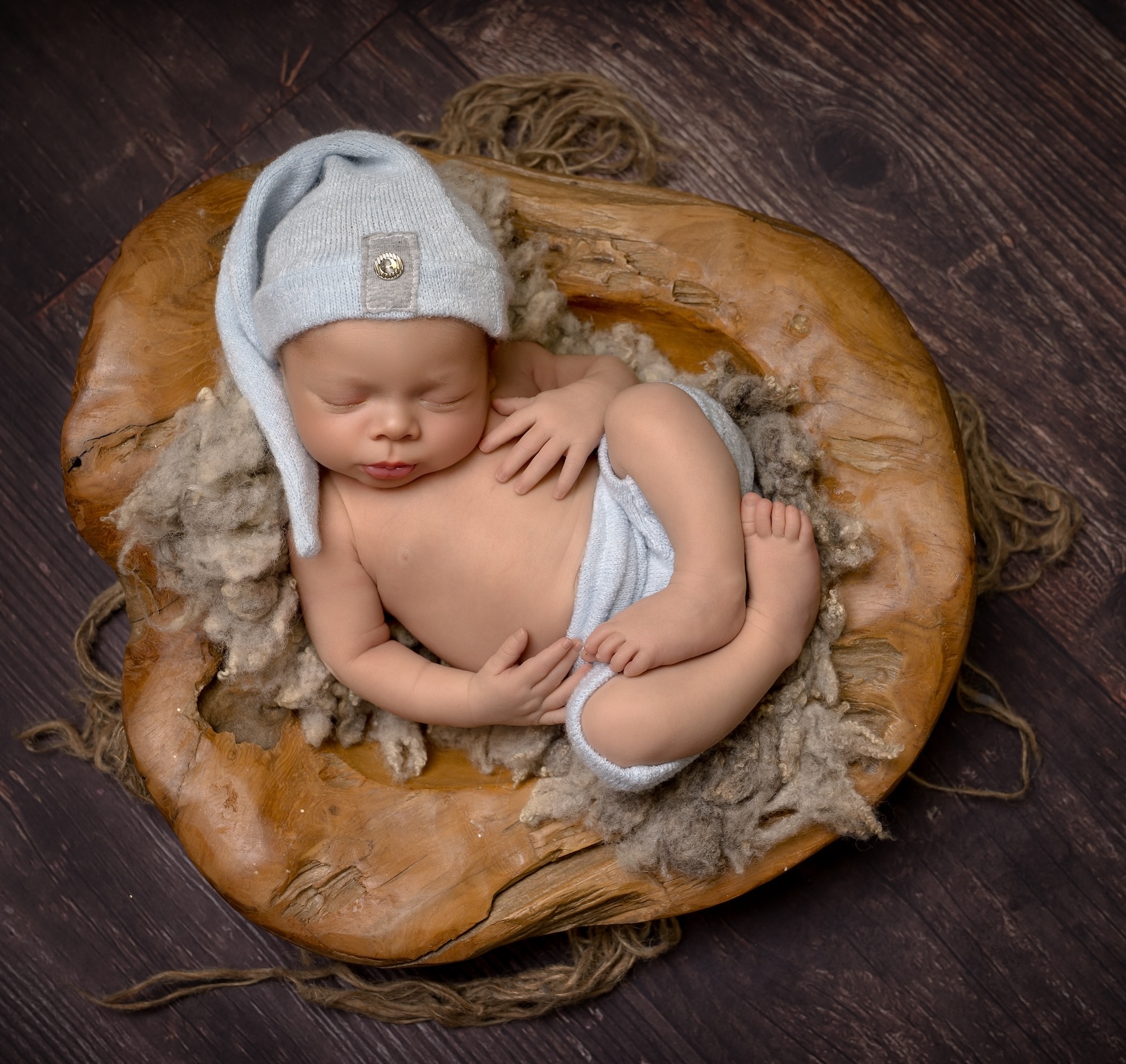 Newborn baby laying in wooden bowl wearing hat by West Sussex photographer