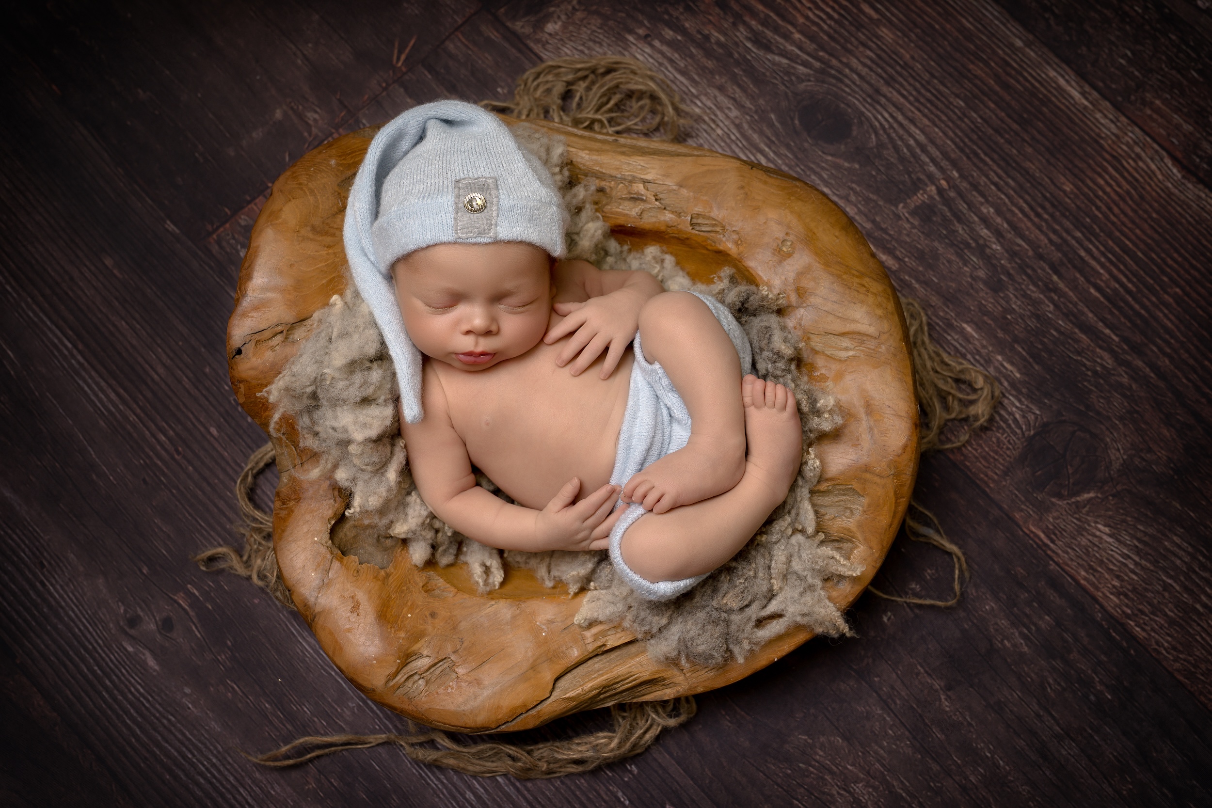 Baby wearing hat laying in wooden bowl by West Sussex photographer