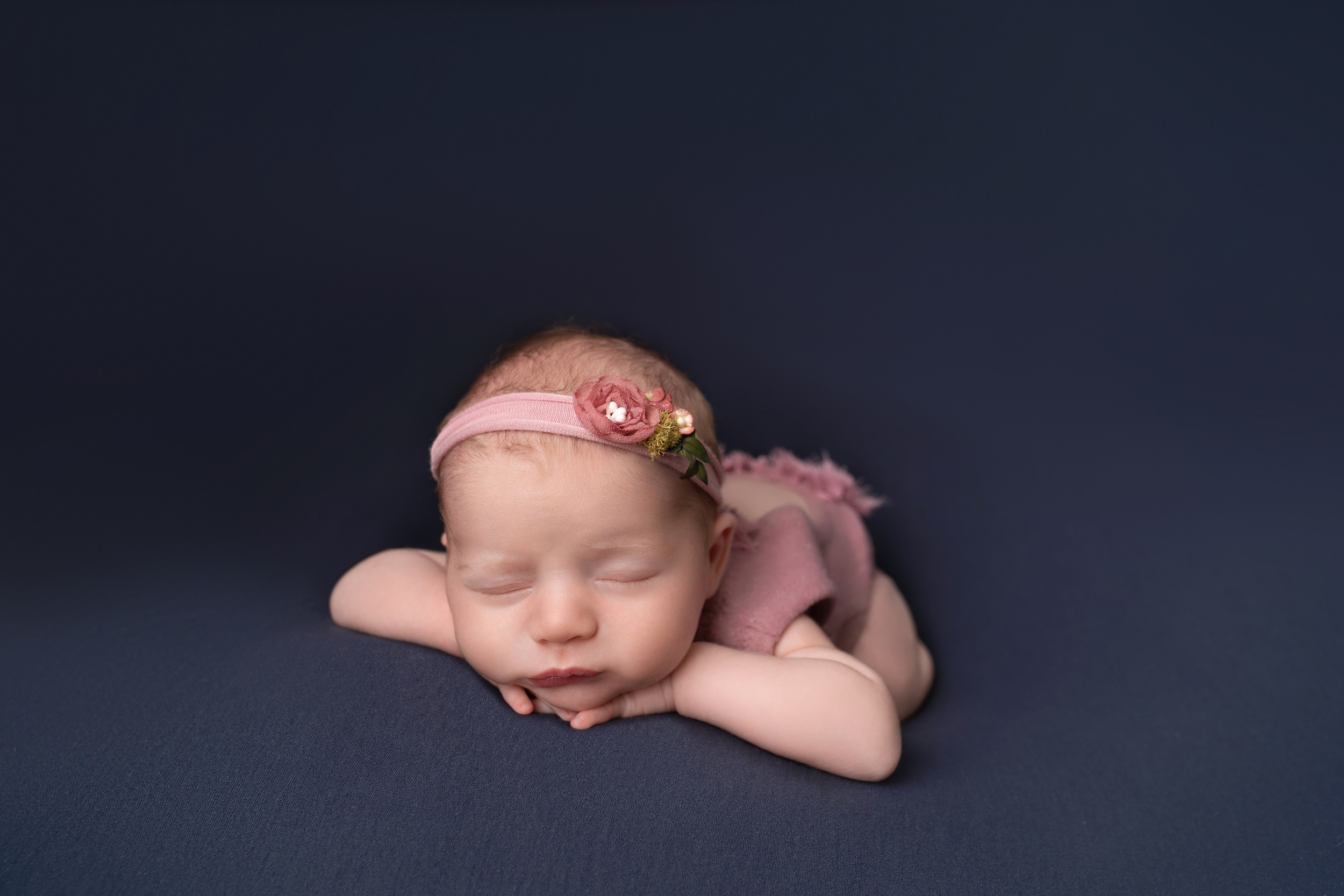 Newborn with head resting on hands and flower headband on by Sussex photographer