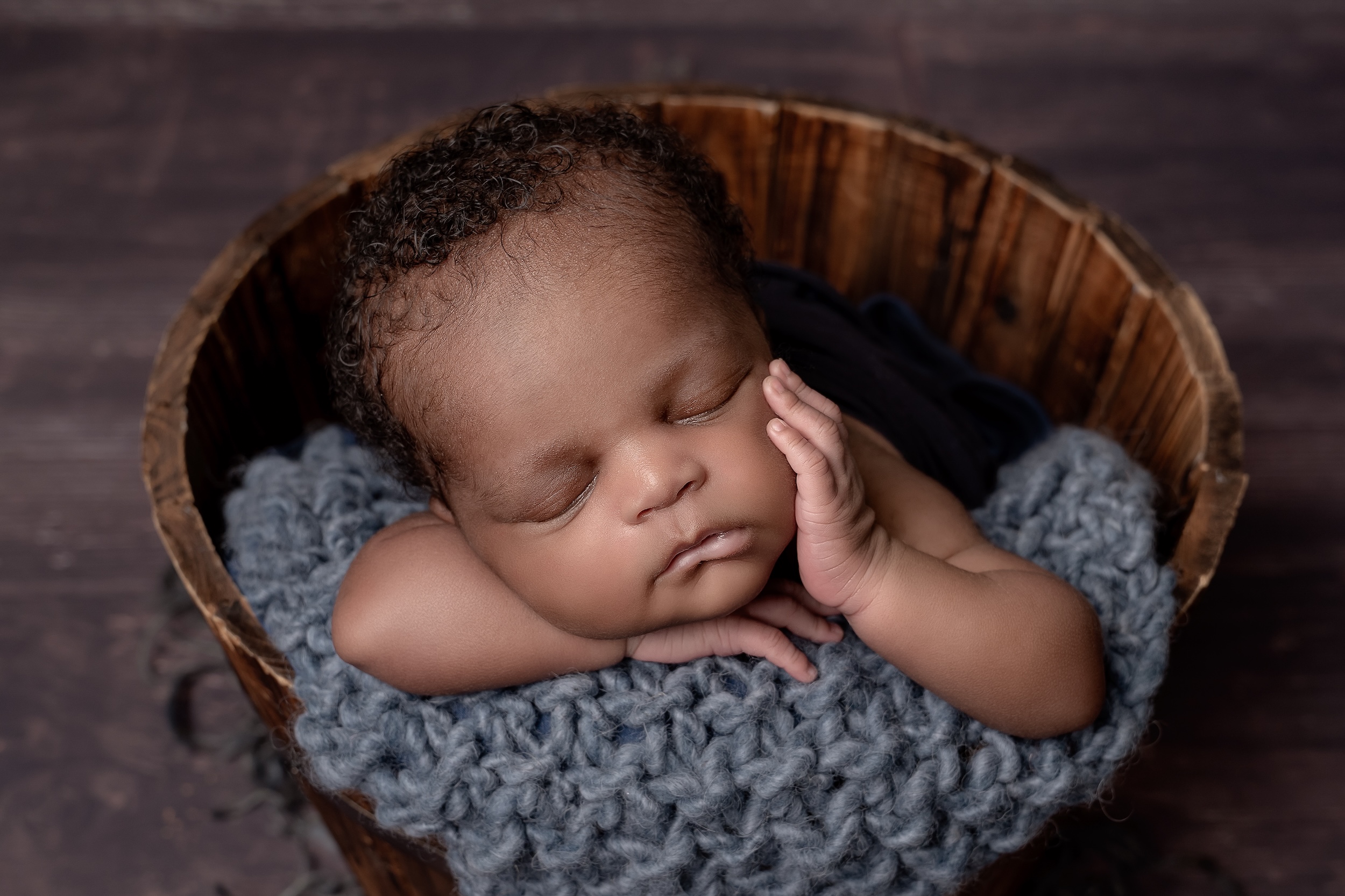 Baby laying in basket with hand on cheek by Crawley photography studio