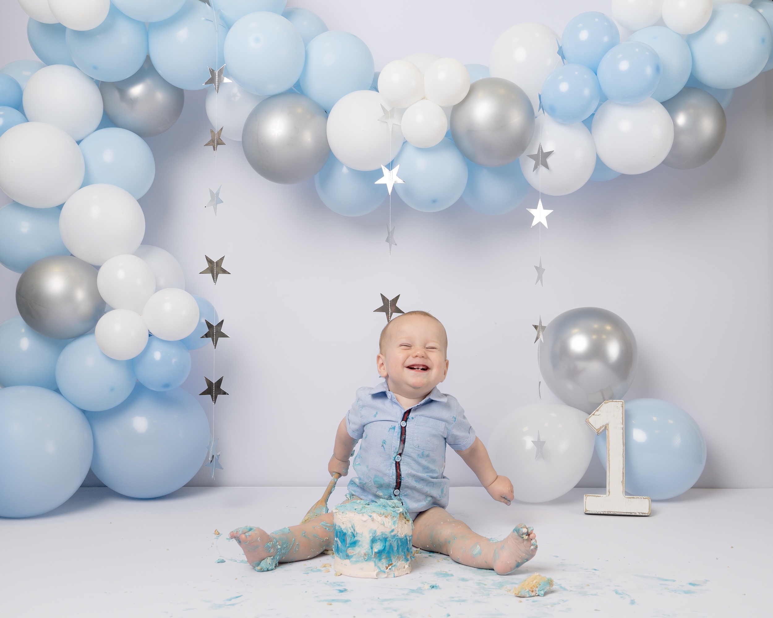 Baby boy with cake in front of balloon arch on first birthday by Forest Row photography studio