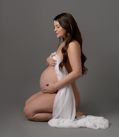 Mother kneeling holding baby bump by Haywards Heath photographer