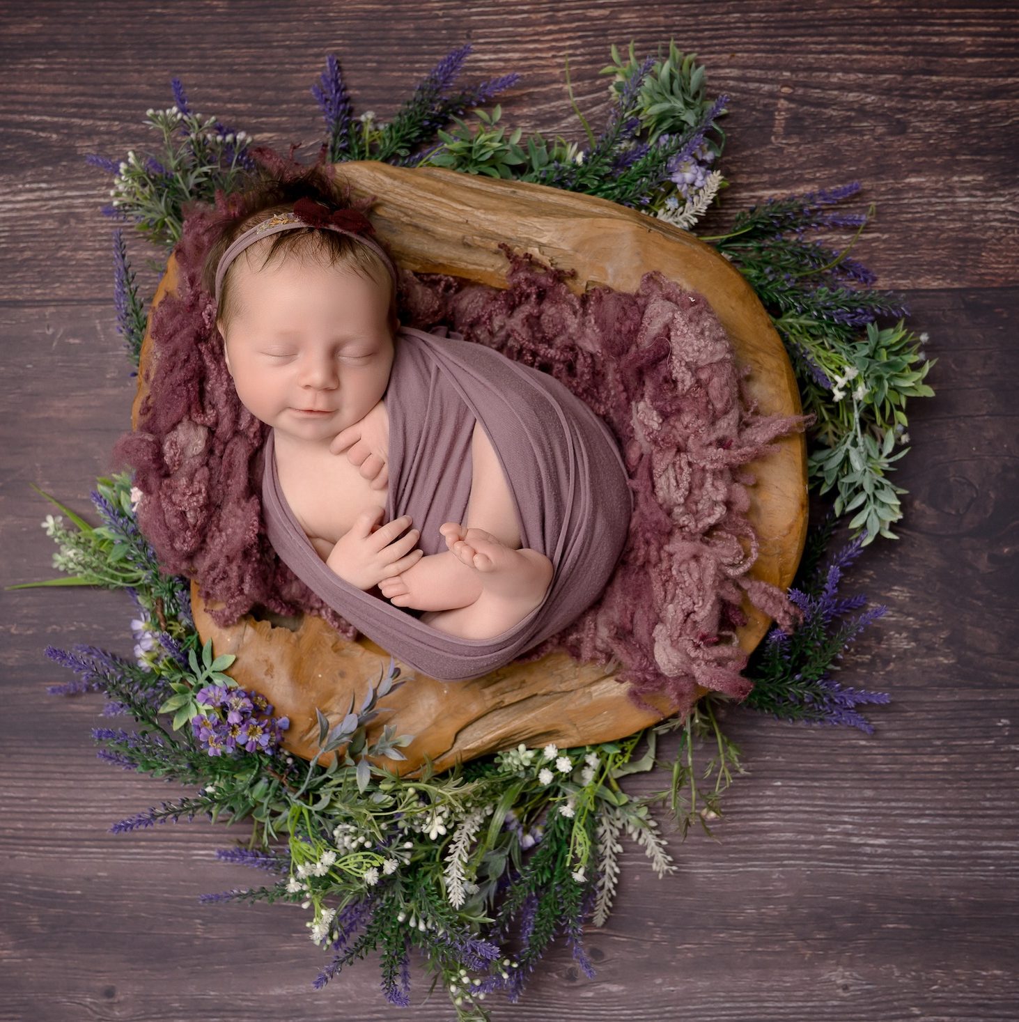 Newborn baby wrapped in balnket surrounded by plants by Crawley photography studio