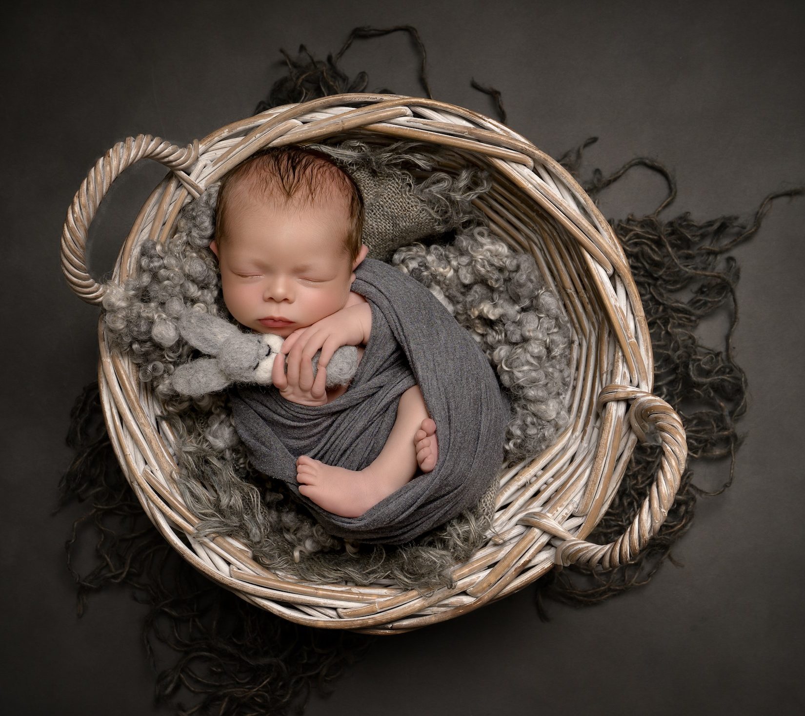 Newborn laying in wooden basket holding bunny wrapped in blanket by Haywards Heath photographer