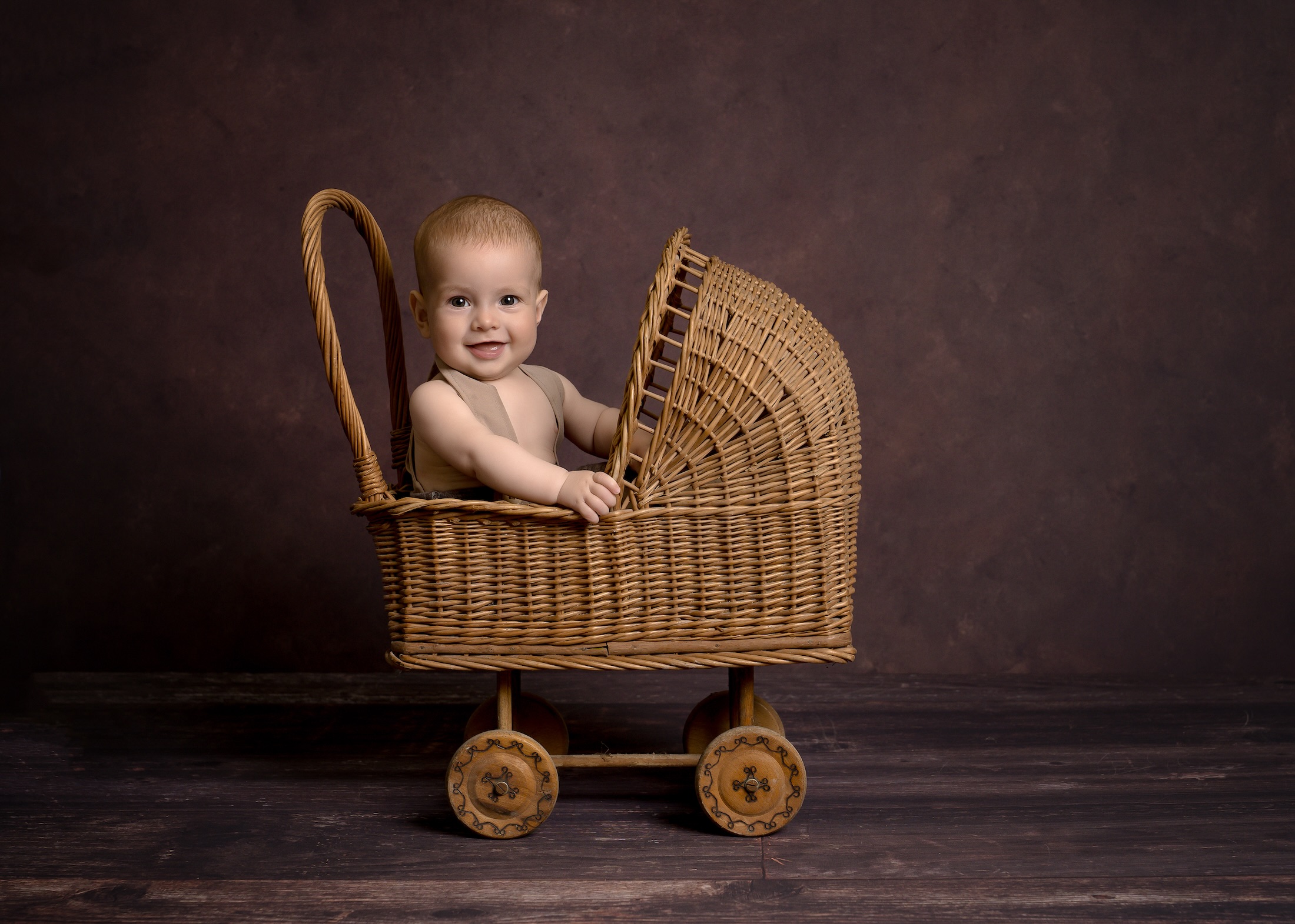 Baby sitting in mini wooden pushchair by Forest Row photographer