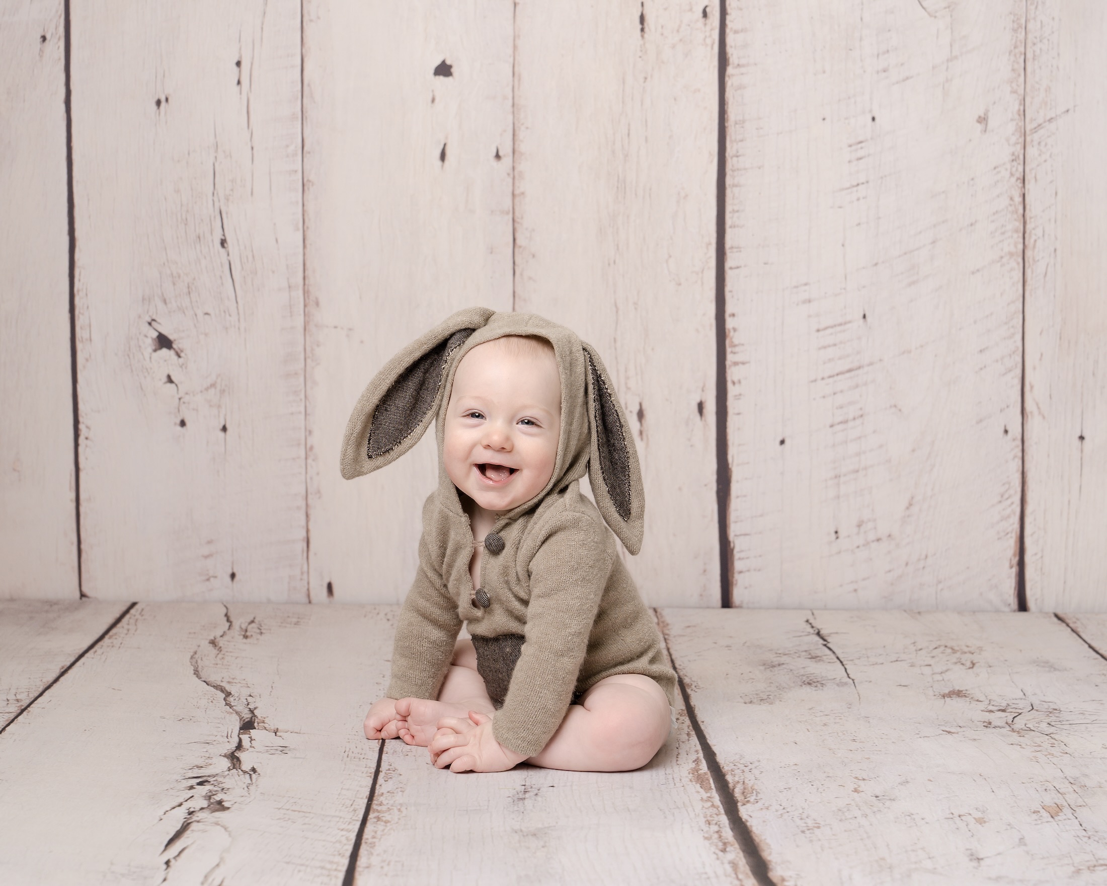 Baby smiling whilst sitting in bunny ear outfit by Haywards Heath photographer