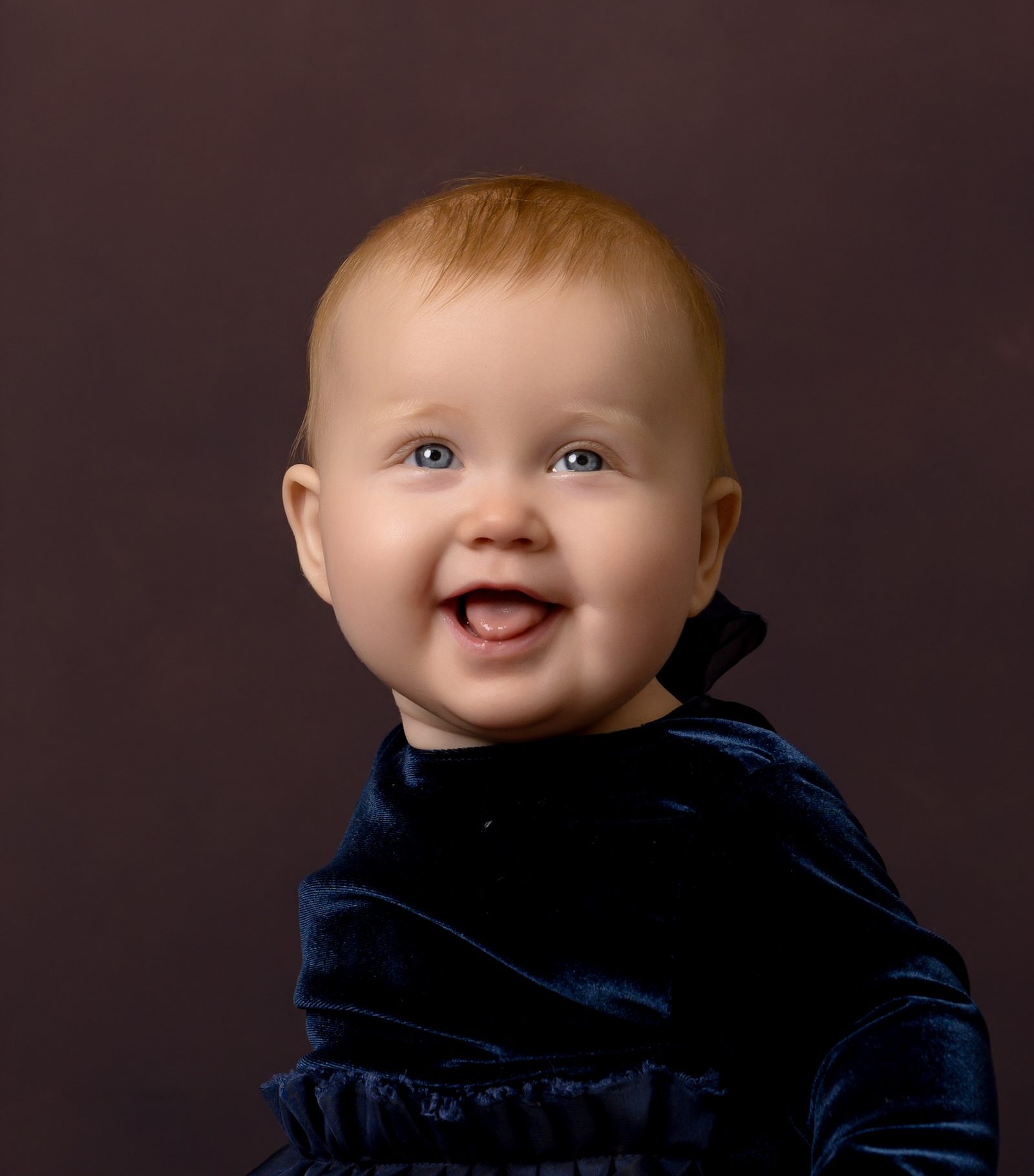 Baby in blue outfit smiling and looking up by East Grinstead photography studio