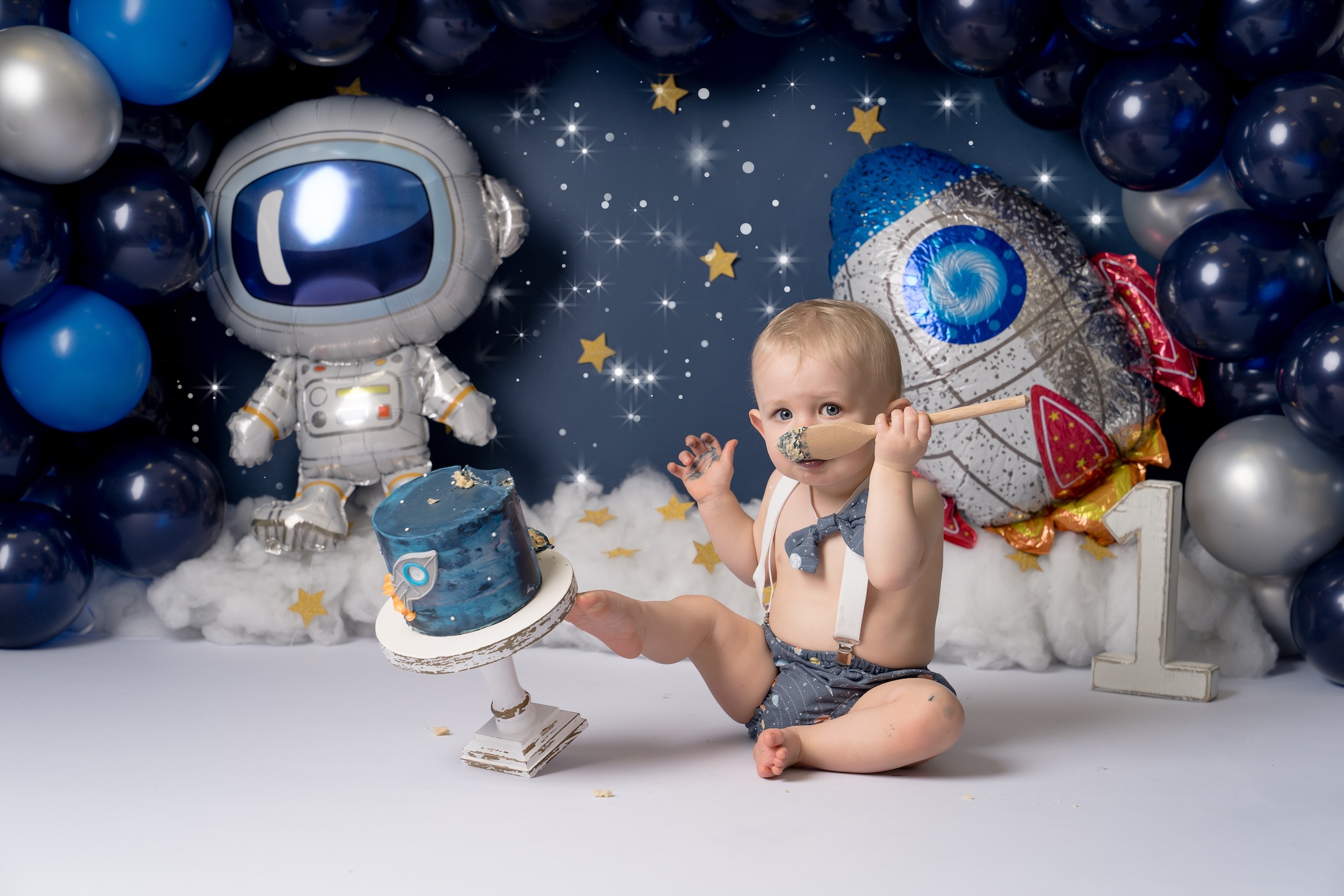 Baby holding wooden spoon kicking space themed cake by Forest Row photographer